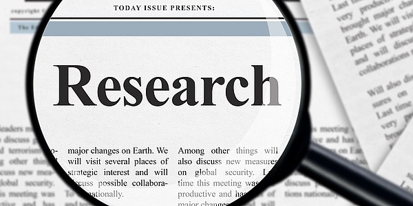 Eine Lupe vergrößert auf einer Zeitung das Wort "Research".