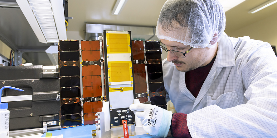 Man in lab coat and hair net works on a cube with folded-out side panels.
