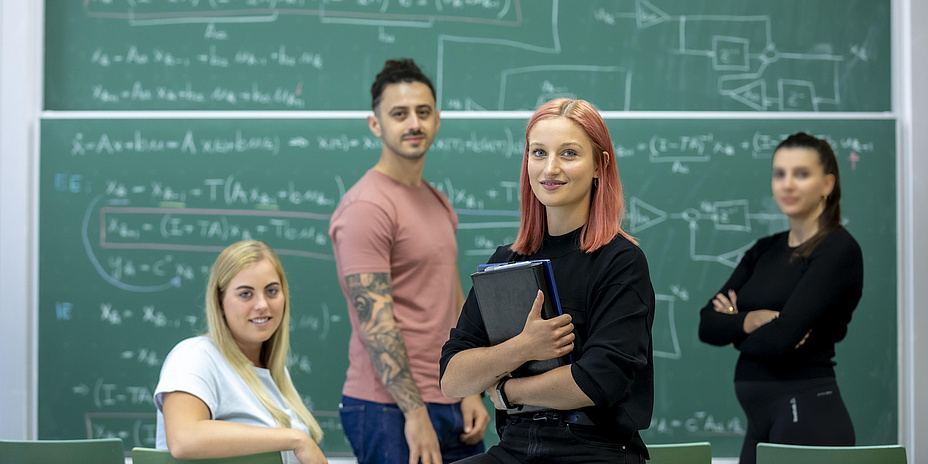 Three young women and a young man in front of a blackboard