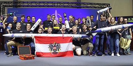 Eine Gruppe von 29 Personen steht auf eine Bühne und hält eine Modellrakete in den Händen.