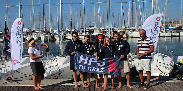 Five students hold HPS flag, sailboats in the background