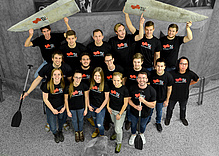 Group photo with TU Graz shirts, paddles and parts of a concrete canoe.