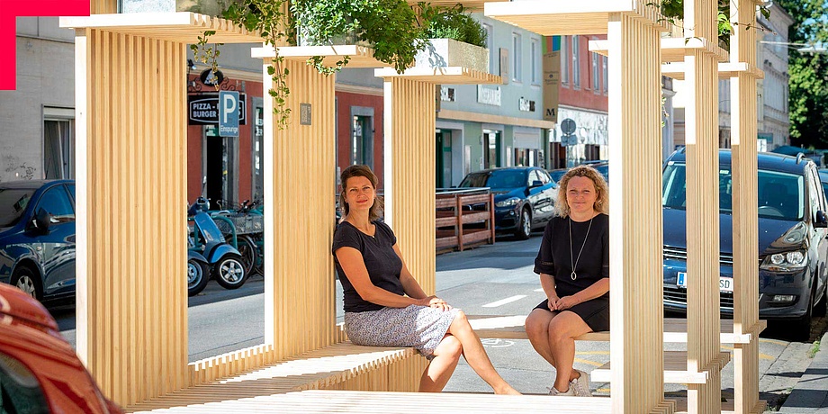 Zwei TU Graz Forscherinnen sitzen in einer temporären Installation (Stadtmöbel) aus Holz