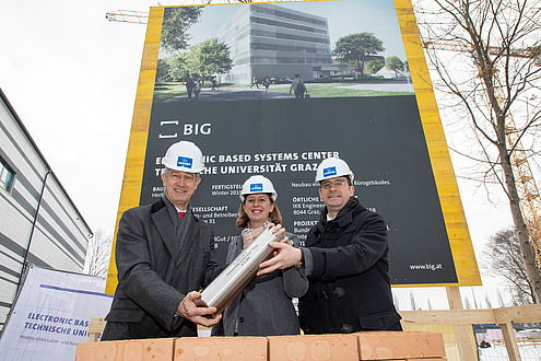 Two men and a woman with construction helmets hold a metal roll.