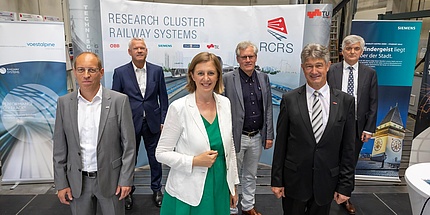 Four gentlemen and a woman in festive dress in front of a wall with railway pictures