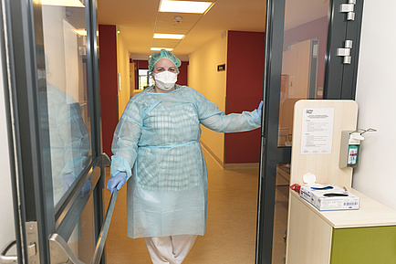 Person in medical protective clothing opens a door.