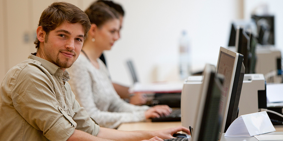 Computerarbeitsraum mit einem jungen Mann im Vordergrund.