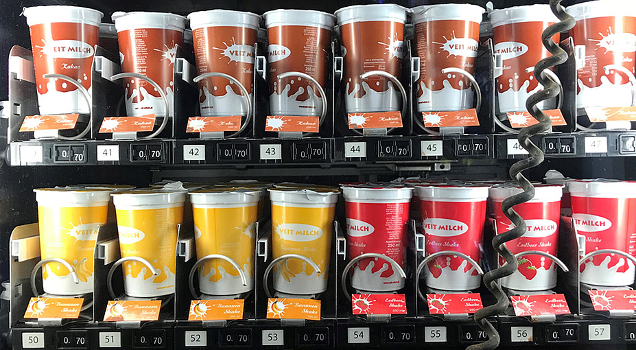 Milch-, Kakao- und Joghurtbecher in Braun, Gelb und Rot mit der Aufschrift „Veit Milch“ im Automaten
