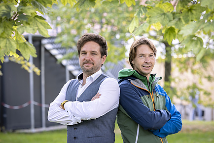 Two men are standing next to each other, lokking into the camera.