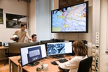 Three people are working at computer screens displaying a geological map.
