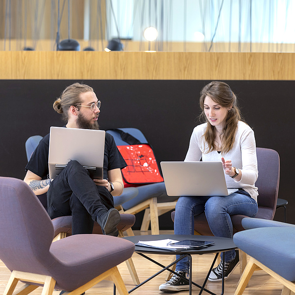 Ein Mann und eine Frau in Loungesesseln mit Laptops am Schoß.