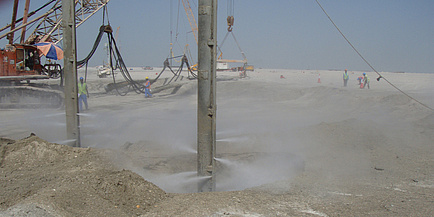 A large pit is enveloped in a cloud of sand; Workers are seen working the soil.