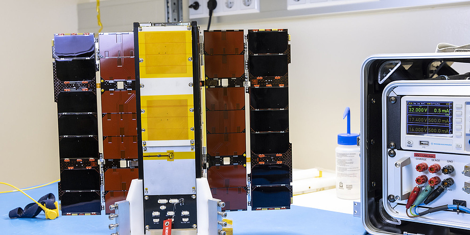 A small satellite with unfolded solar sails stands on a table.