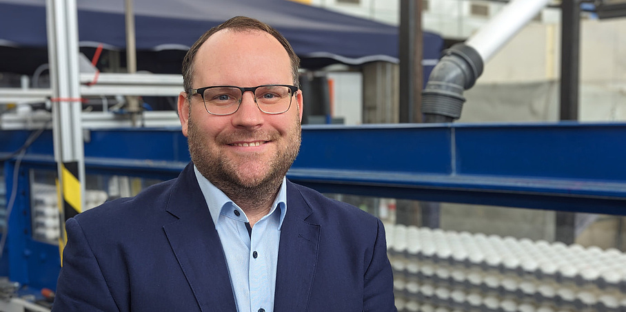 Ein lächelnder Mann steht vor Metallstreben.