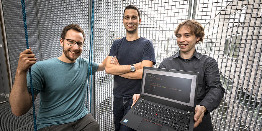 Moritz Lipp, Michael Schwarz and Daniel Gruss. Daniel Gruss holds a laptop computer with white text written on a black screen.