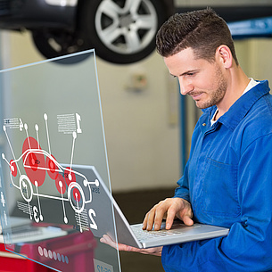 Ein Mann mit Laptop vor einer Glastafel, auf der ein Auto mit Informationstext abgebildet ist. Bildquelle: vektorfusioniert – Fotolia.com