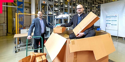 Zwei Männer im Anzug mit Papierschachteln in Logistikzentrum.