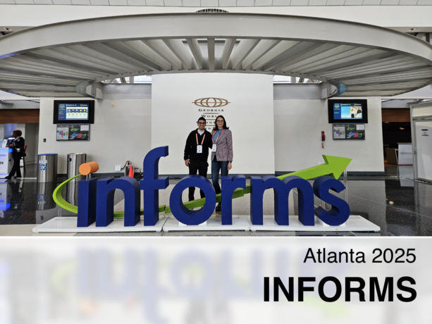 Zwei Personen posieren hinter einem großen blauen „INFORMS“-Schriftzug mit grünem Pfeil im Georgia World Congress Center in Atlanta 2025, flankiert von Bildschirmen in einer modernen Halle.