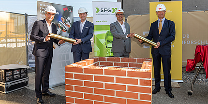 Four men with construction helmets in front of a wall with foundation stone rolls