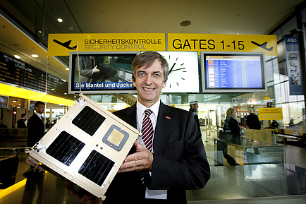 Otto Koudelka mit einem 1:1 Modell des Nanosatelliten TUGSAT-1 am Flughafen Graz-Thalerhof.