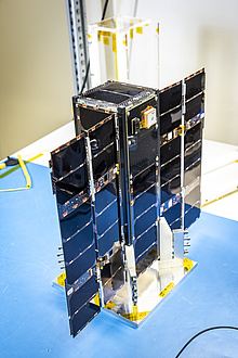 A small satellite with unfolded solar sails stands on a table.
