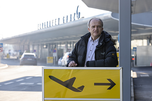 Mann vor einem Schild mit einem startenden Flugzeug. 