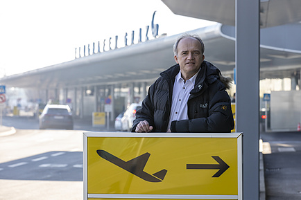 Man in front of a sign with a plane taking off. 