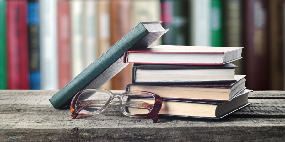 Pile of books and pair of glasses on wooden shelf