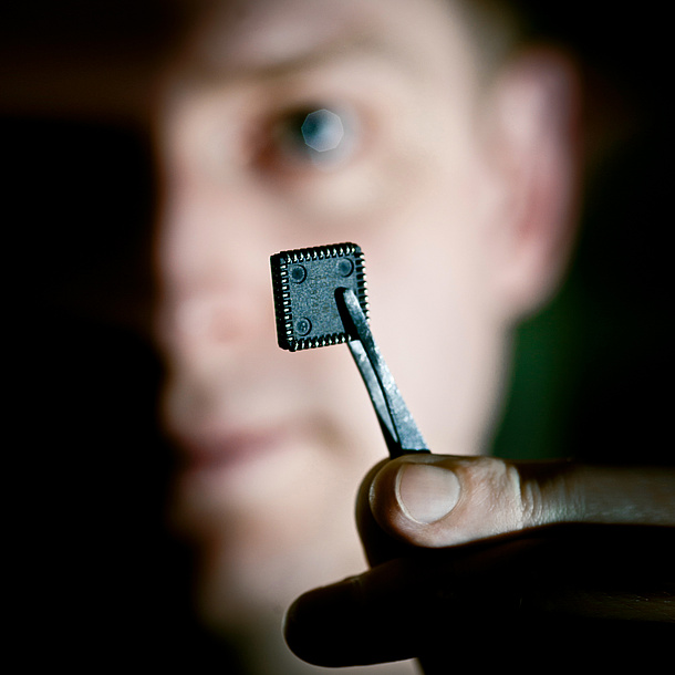 Ein Mann hält mit einer Pinzette einen Chip. Bildquelle: Lunghammer – TU Graz