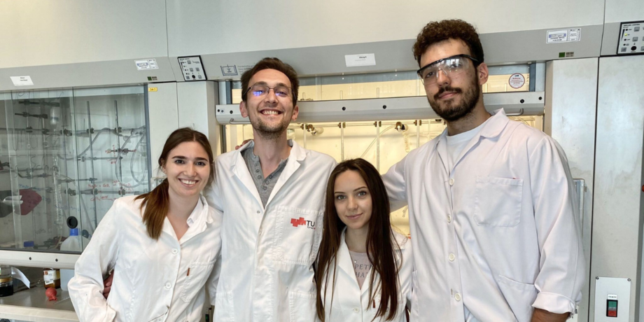 A group of students stands in an office in lab coats.