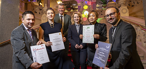 Drei lächelnde Männer und drei Frauen stehen zusammen, vier von ihnen halten Urkunden.