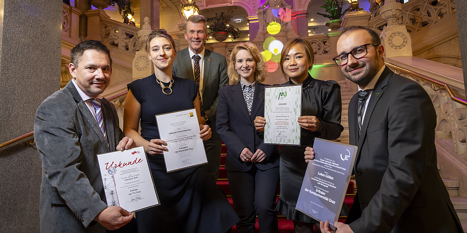 Three smiling men and three women stand together, four of them holding certificates