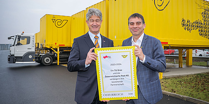 Zwei Männer halten ein Schild in die Kamera, das über die Verlängerung der Kooperation zwischen TU Graz und Österreichische Post AG informiert