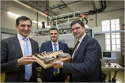 The picture shows three gentlemen holding a board with material samples into the camera.