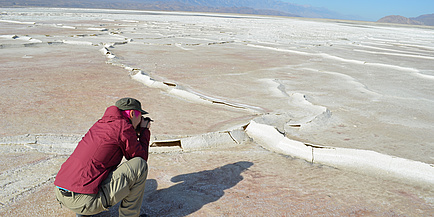 Woman squats on the ground and looks at raised structures on the ground.