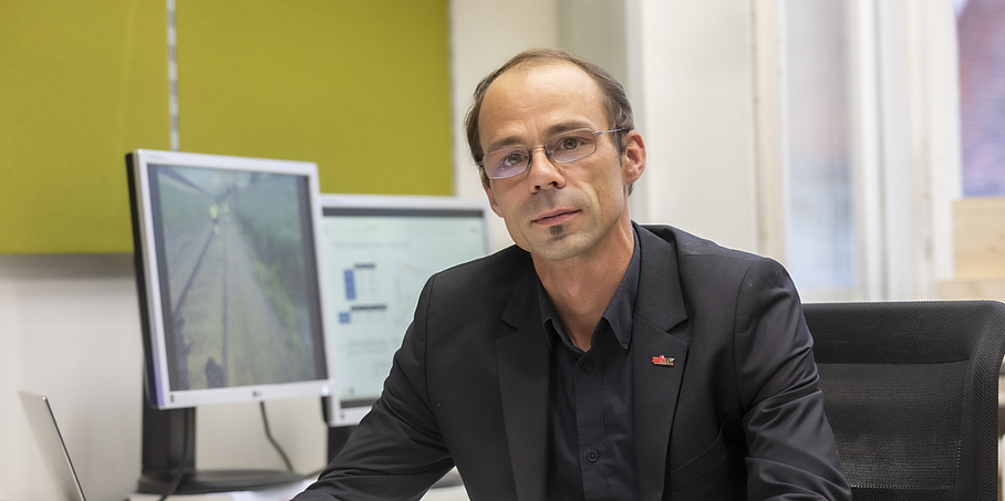 Ein Mann mit Brille sitzt an einem Schreibtisch und schaut in die Kamera.