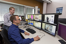 Two men in front of a total of six computer screens showing various graphic models.
