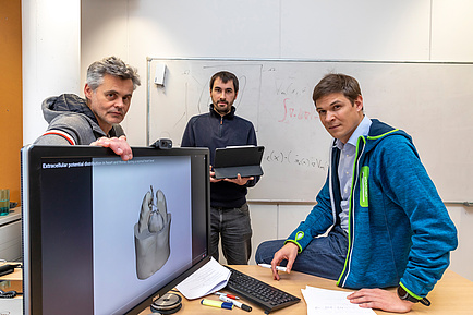 Drei Herren vor einem Computerbildschirm, ein digitales Herz ist abgebildet