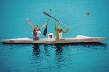Two cheering women in a concrete canoe on water.