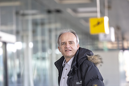 Lächelnder Mann, im Hintergrund ein Schild mit einem landenden Flugzeug.