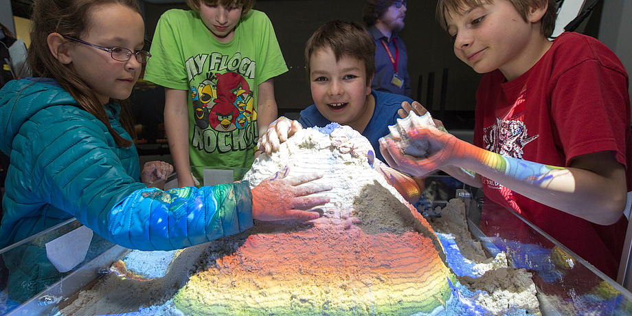 Vier Kinder spielen mit einem bunt beleuchteten Sandhaufen.