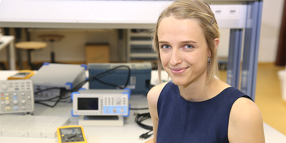 Junge Frau vor einem Tisch mit elektronischen Geräten.