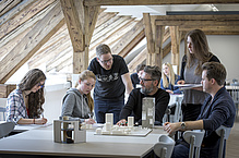 Studierendengruppe mit Lehrperson vor Architekturmodellen.