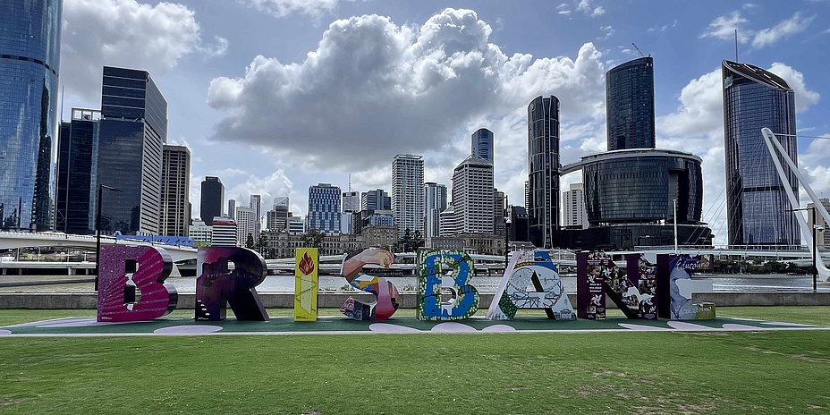 Sculpture with colourful letters forming the word Brisbane. Behind it, many skyscrapers towering into the blue sky with a few clouds.