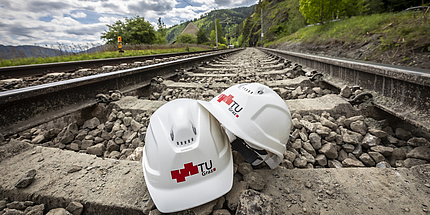 Zwischen zwei Schienen liegen zwei Helme mit dem TU Graz-Logo.