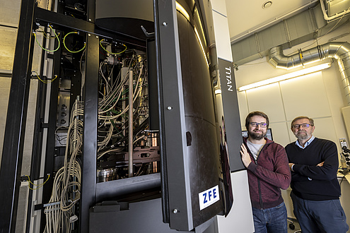 Two men stand next to a box-shaped machine with many cables visible inside.