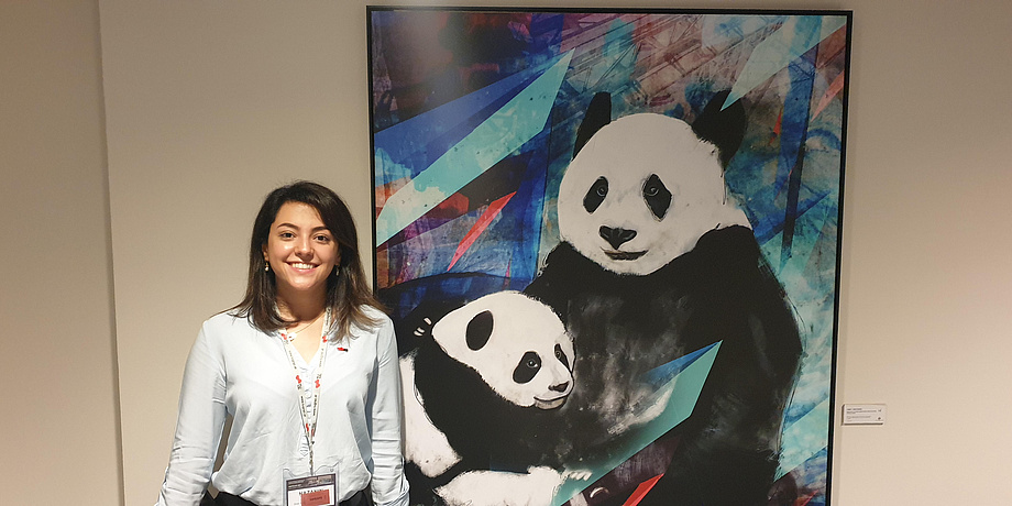 Young, dark-haired woman with name tag in front of big painting with pandas.