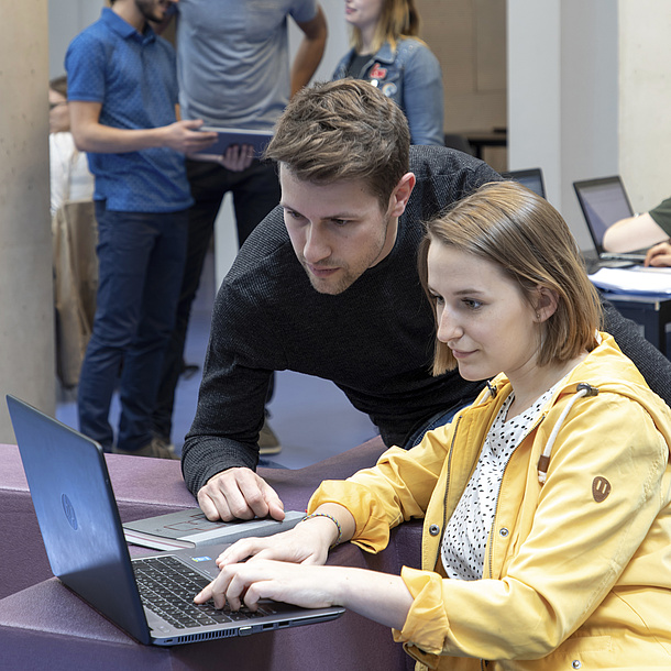 Eine junge Frau und ein junger Mann blicken in einen Laptop.