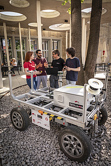 Four people stand behind a four-wheeled robot.