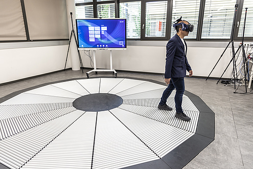 Ein Mann mit einer VR-Brille auf dem Kopf bewegt sich über einen Boden mit Rollen.